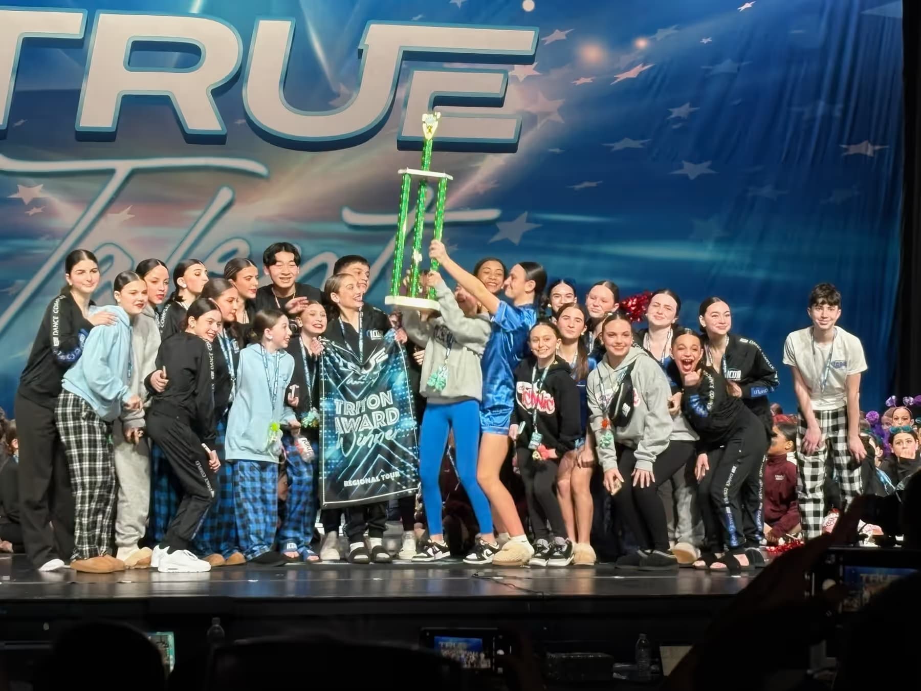 Icon team dancers holding a trophy on stage.